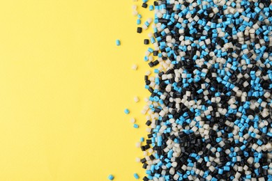 Photo of Pile of colorful plastic granules on yellow background, top view. Space for text