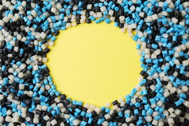 Photo of Frame of colorful plastic granules on yellow background, top view. Space for text