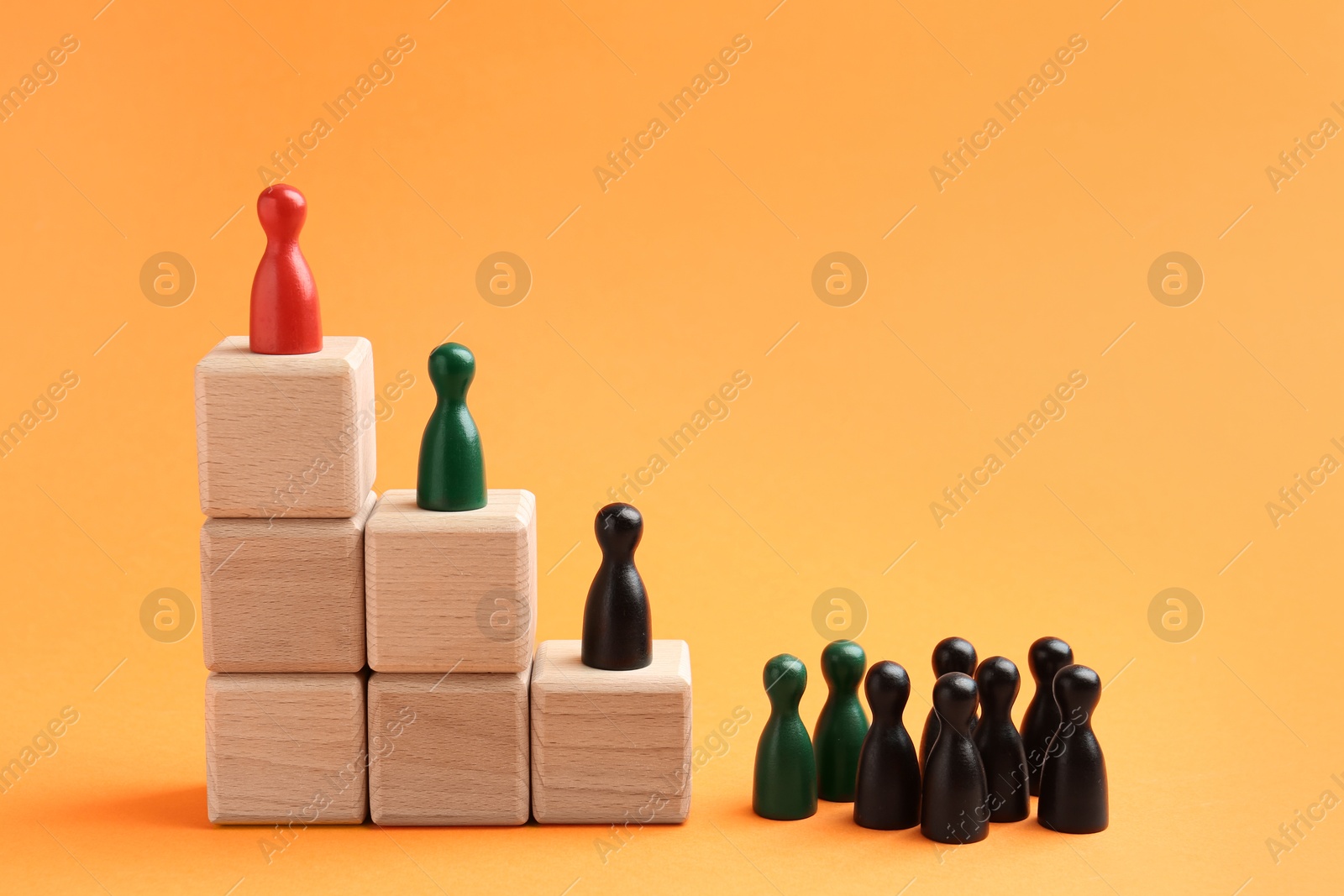 Photo of Human figures, red one on top of stacked wooden cubes against orange background. Competition concept