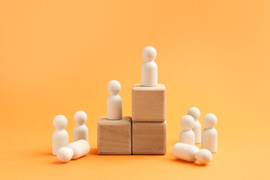 Photo of Human figures on stacked wooden cubes against orange background. Competition concept