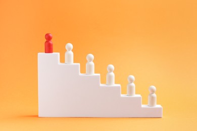 Photo of Human figures on stairs, red one on top against orange background. Competition concept