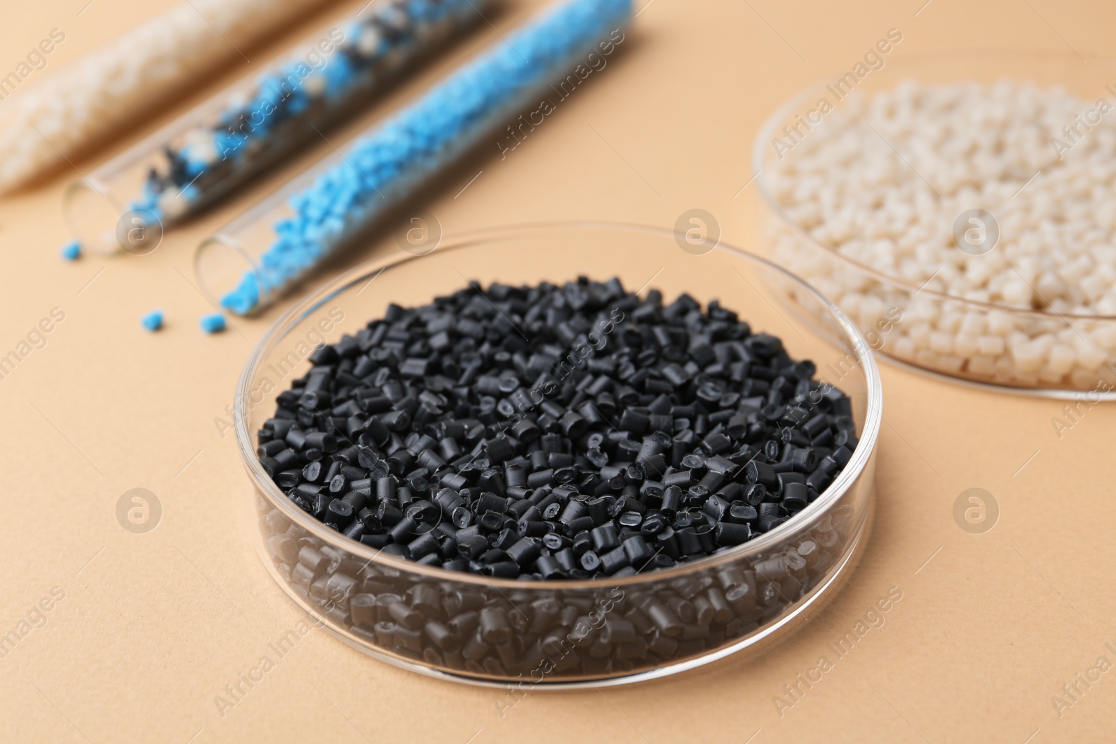 Photo of Colorful plastic granules in petri dishes and test tubes on beige background, closeup