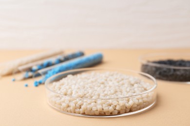 Photo of Colorful plastic granules in petri dishes and test tubes on beige background, selective focus. Space for text