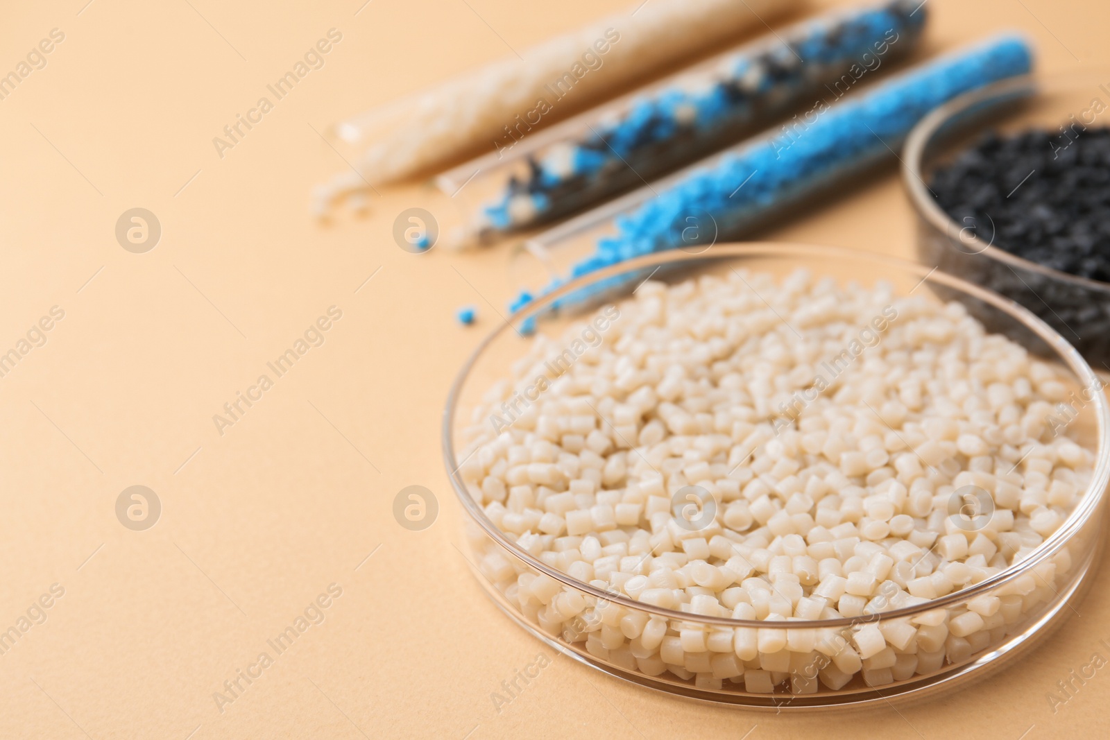 Photo of Colorful plastic granules in petri dishes and test tubes on beige background, closeup. Space for text