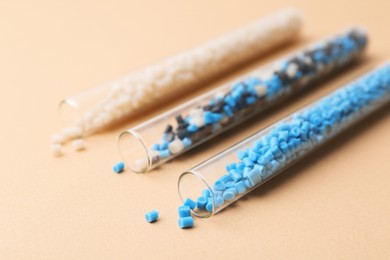 Photo of Colorful plastic granules in test tubes on beige background, closeup