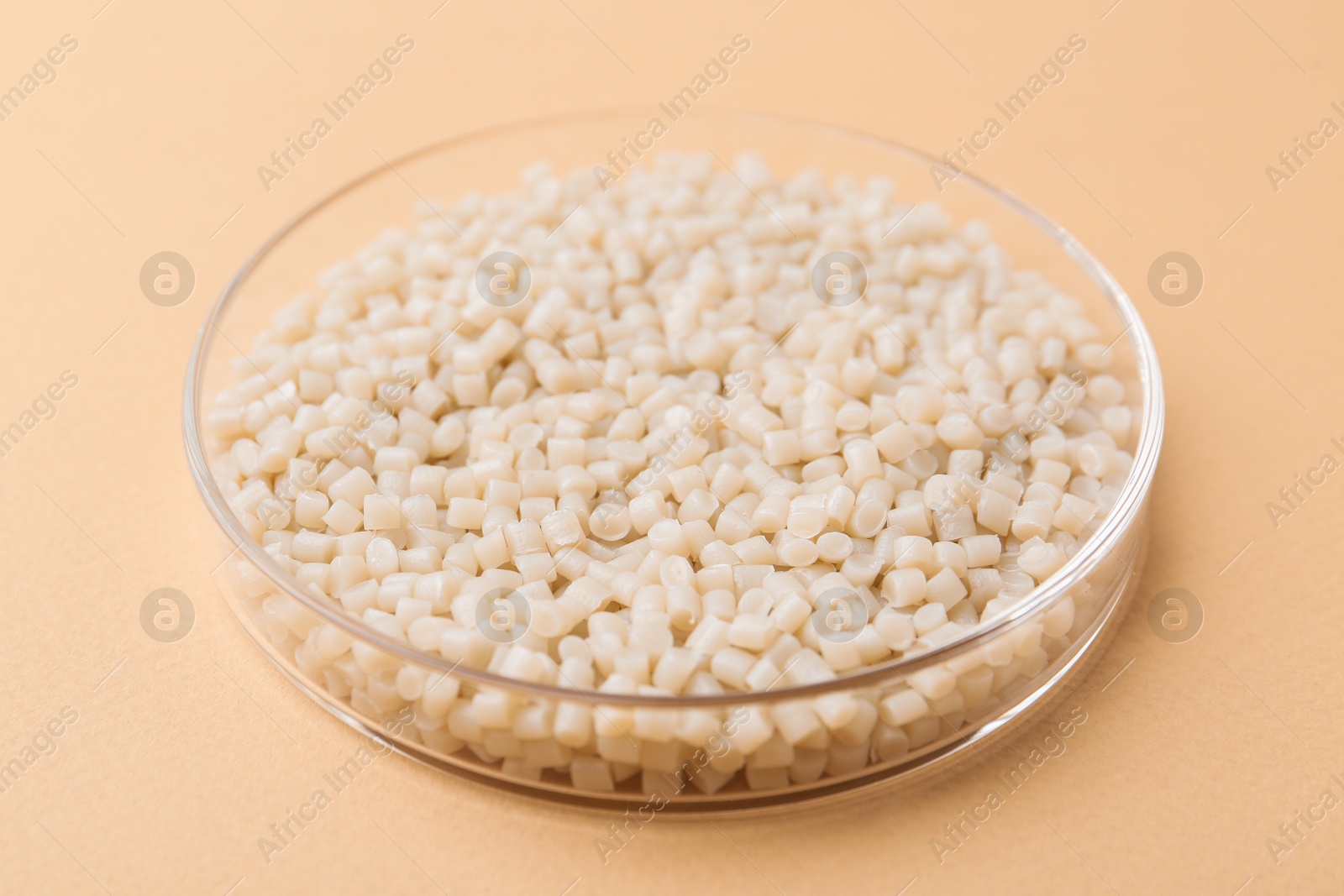 Photo of Plastic granules in petri dish on beige background, closeup