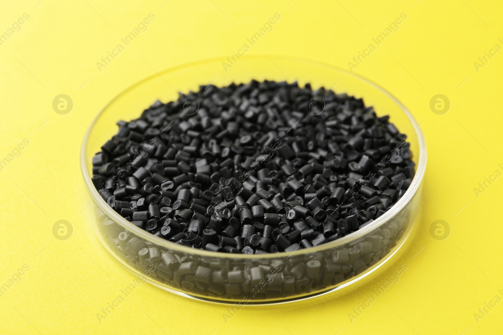 Photo of Black plastic granules in petri dish on yellow background, closeup