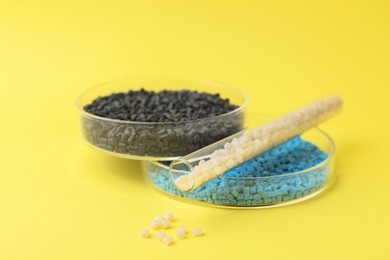 Photo of Colorful plastic granules in petri dishes and test tube on yellow background, closeup