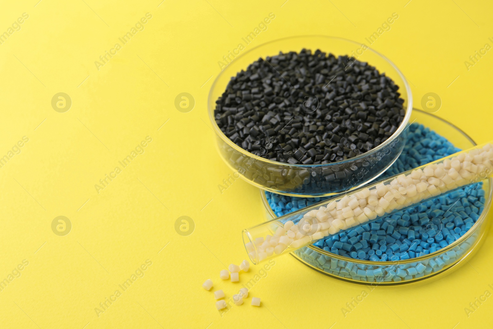 Photo of Colorful plastic granules in petri dishes and test tube on yellow background, closeup. Space for text