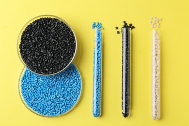 Photo of Colorful plastic granules in petri dishes and test tubes on yellow background, flat lay