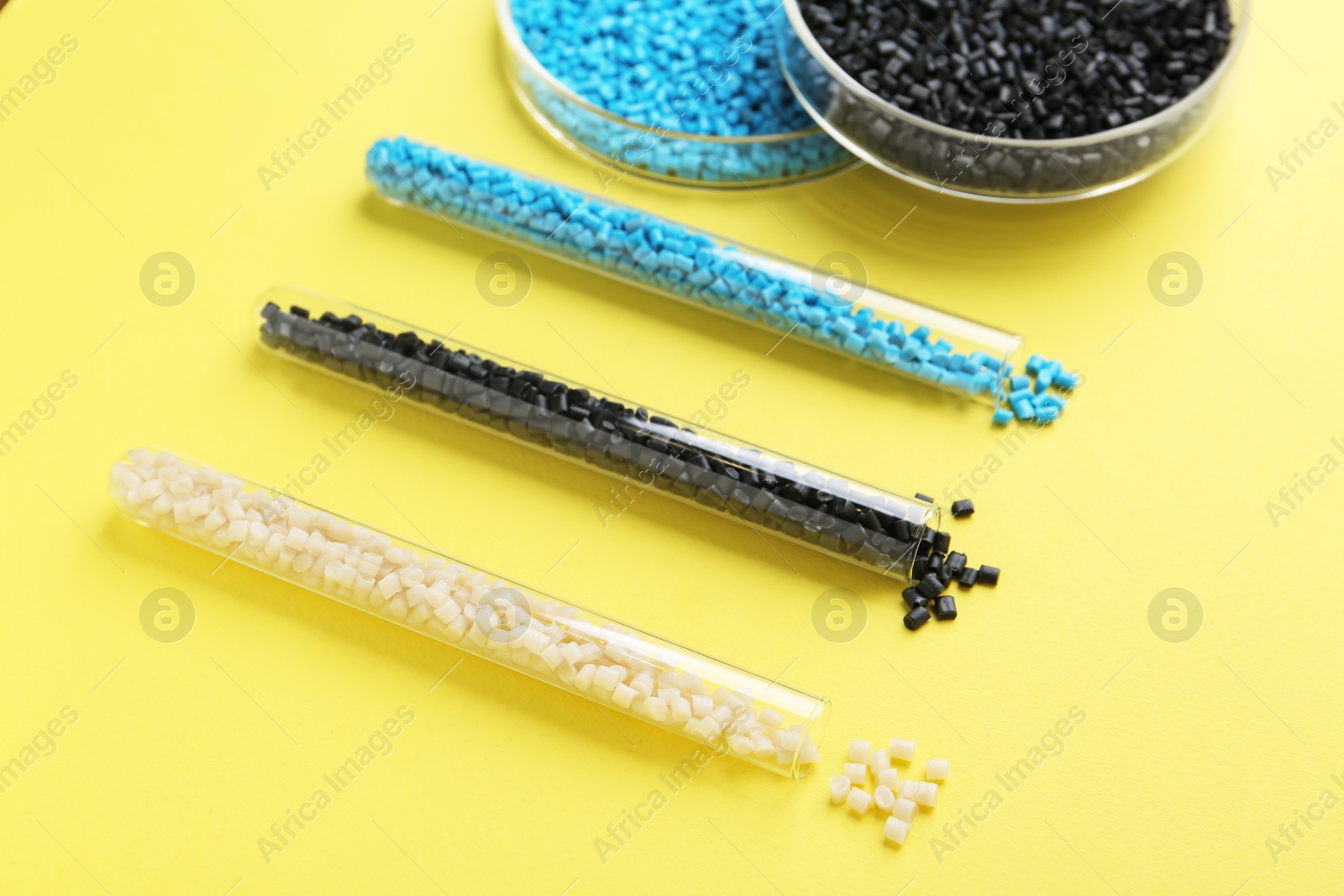 Photo of Colorful plastic granules in petri dishes and test tubes on yellow background, closeup