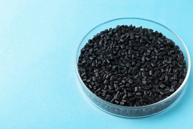 Photo of Black plastic granules in petri dish on light blue background, closeup. Space for text