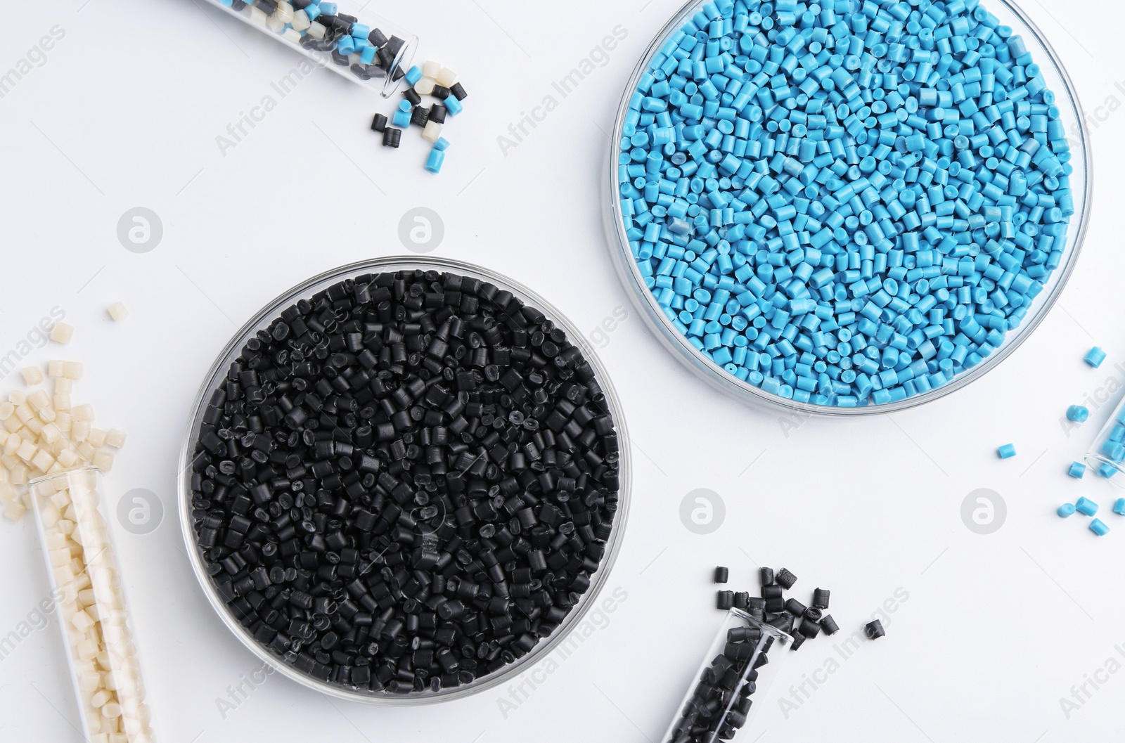 Photo of Colorful plastic granules in petri dishes and test tubes on white background, flat lay