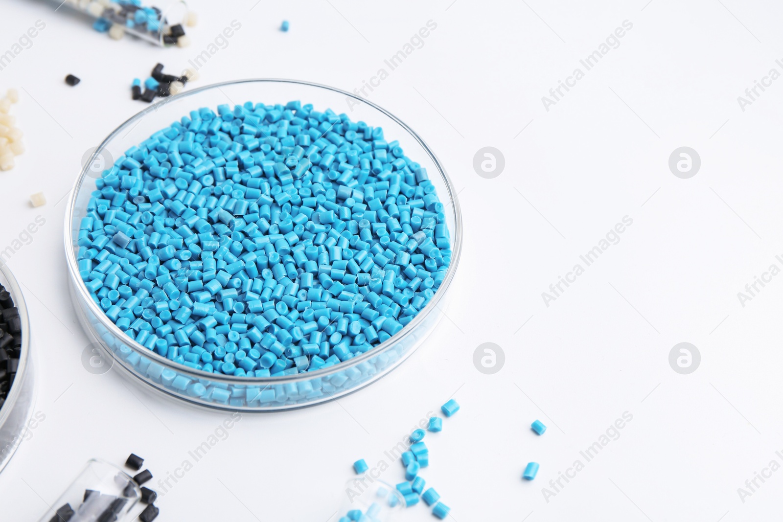 Photo of Colorful plastic granules in petri dish and test tubes on white background, closeup. Space for text