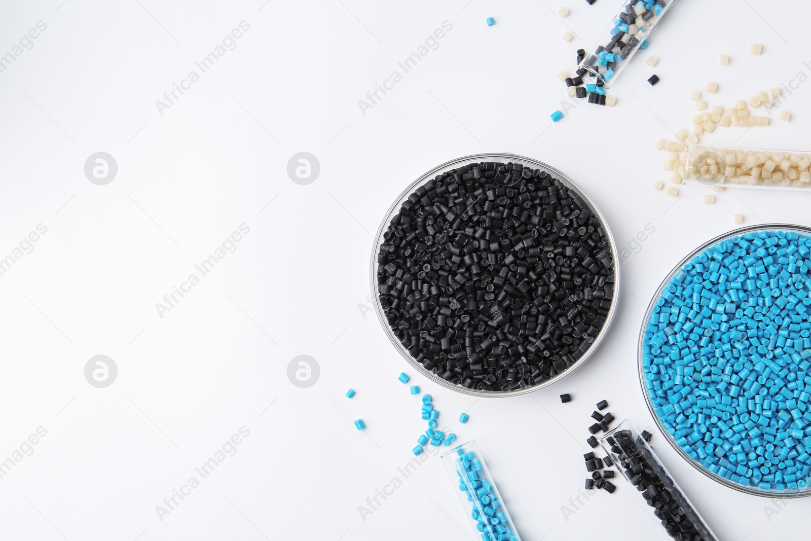 Photo of Colorful plastic granules in petri dishes and test tubes on white background, flat lay. Space for text