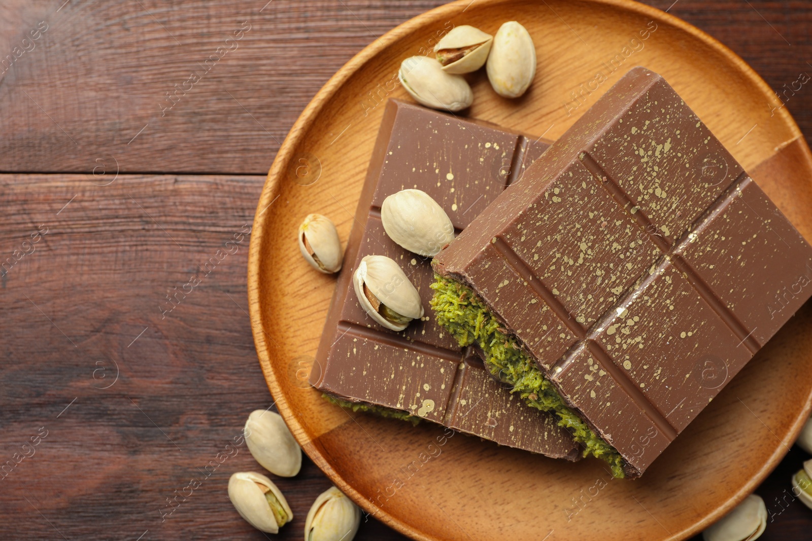 Photo of Pieces of tasty Dubai chocolate with pistachios and knafeh on wooden table, flat lay. Space for text