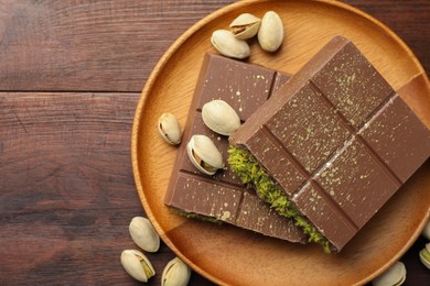 Photo of Pieces of tasty Dubai chocolate with pistachios and knafeh on wooden table, flat lay. Space for text