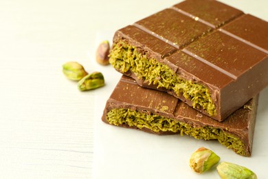 Photo of Pieces of tasty Dubai chocolate with pistachios and knafeh on white wooden table, closeup. Space for text