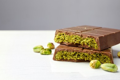 Photo of Pieces of tasty Dubai chocolate with pistachios and knafeh on white wooden table, closeup. Space for text