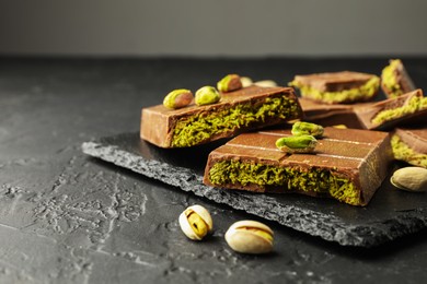 Photo of Pieces of Dubai chocolate bars with pistachios and knafeh on grey table, closeup. Space for text