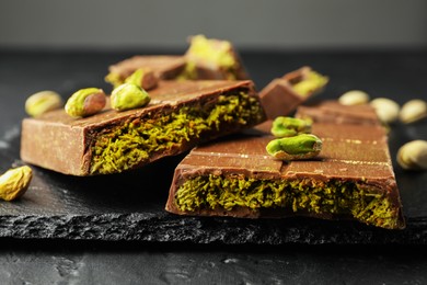 Photo of Pieces of Dubai chocolate bars with pistachios and knafeh on grey table, closeup