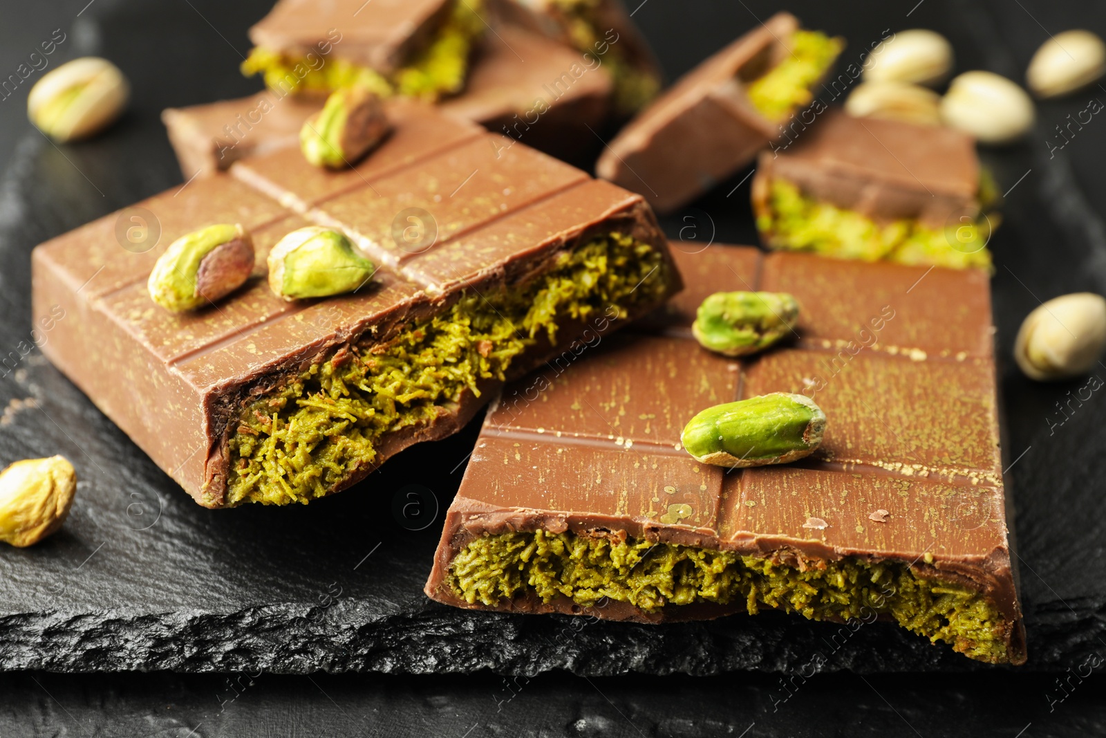 Photo of Pieces of Dubai chocolate bars with pistachios and knafeh on grey table, closeup