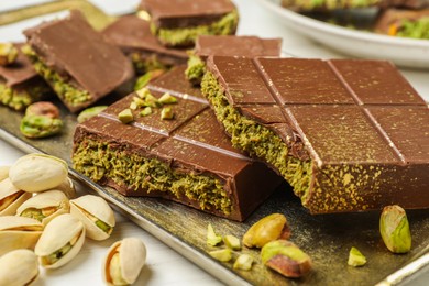 Photo of Pieces of Dubai chocolate bars with pistachios and knafeh on white table, closeup