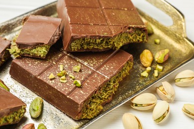 Photo of Pieces of Dubai chocolate bars with pistachios and knafeh on white wooden table, closeup