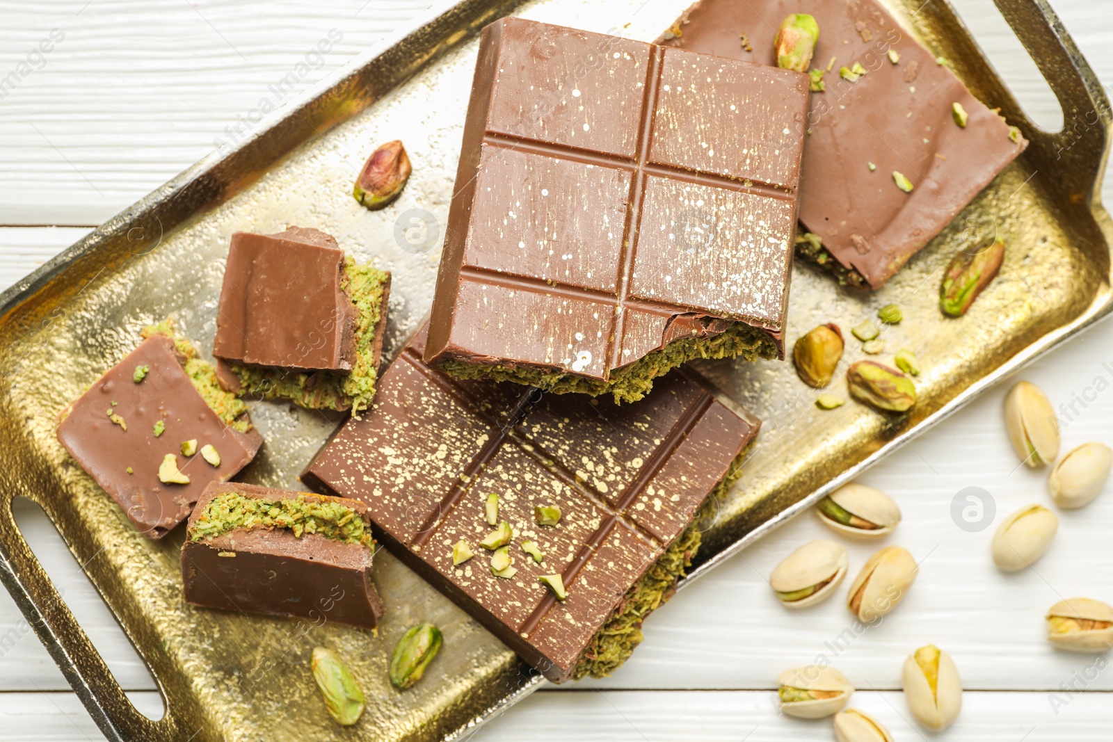 Photo of Pieces of Dubai chocolate bars with pistachios and knafeh on white wooden table, flat lay