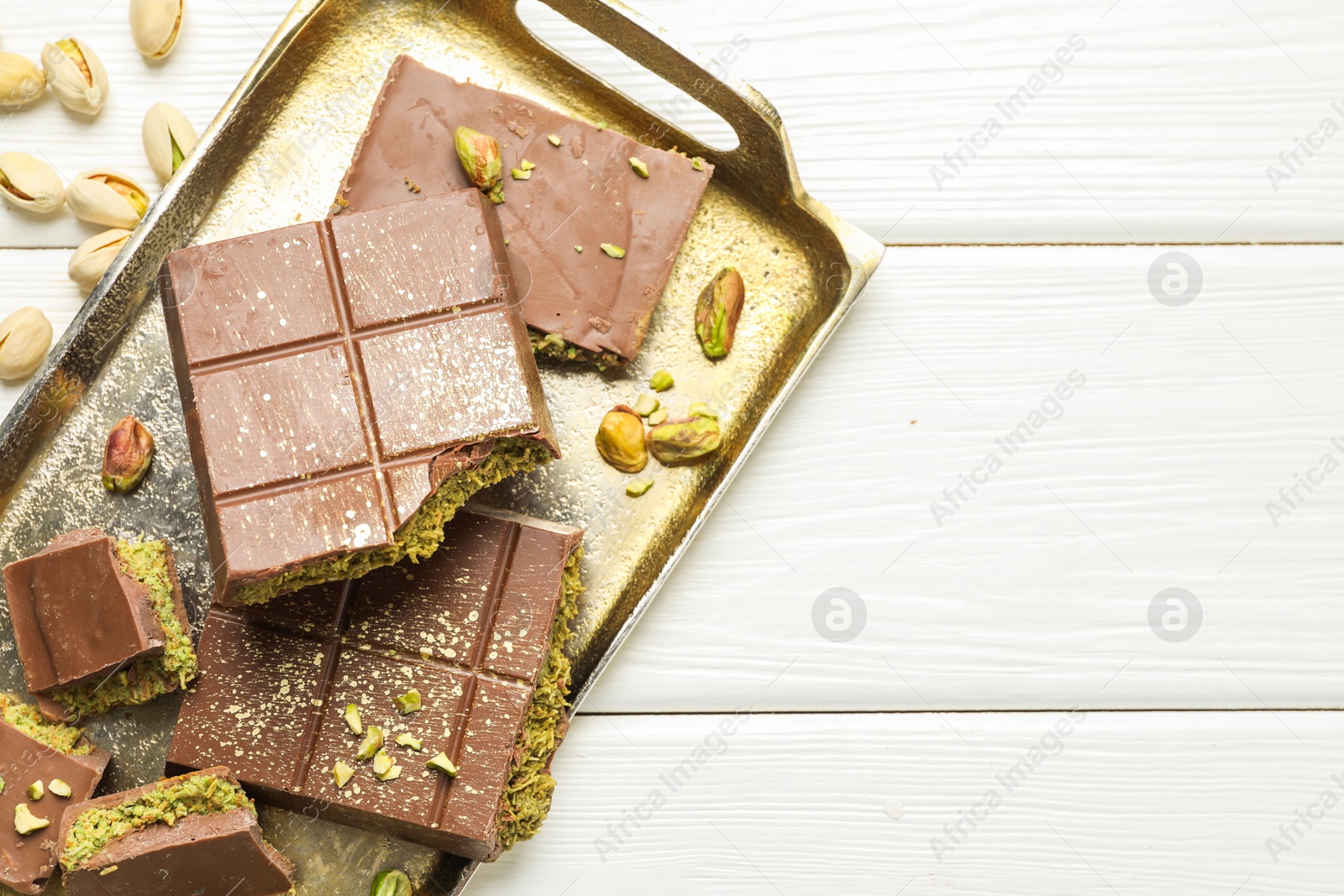 Photo of Pieces of Dubai chocolate bars with pistachios and knafeh on white wooden table, top view. Space for text