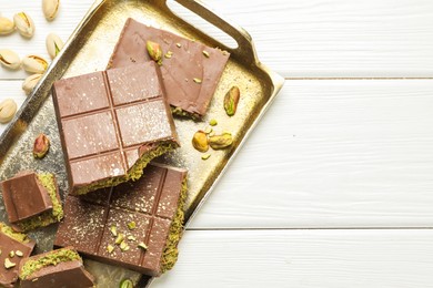 Photo of Pieces of Dubai chocolate bars with pistachios and knafeh on white wooden table, top view. Space for text