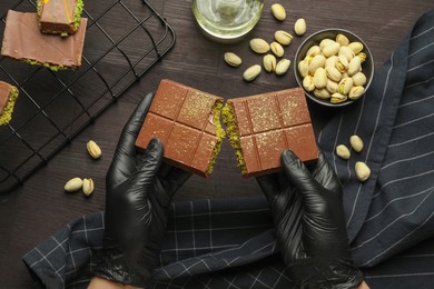 Photo of Woman breaking Dubai chocolate bar with pistachios and knafeh at wooden table, top view