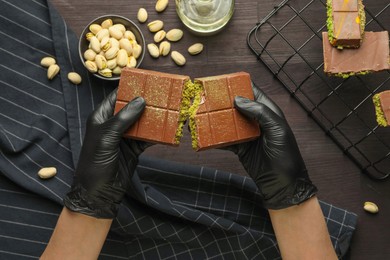 Photo of Woman breaking Dubai chocolate bar with pistachios and knafeh at wooden table, top view