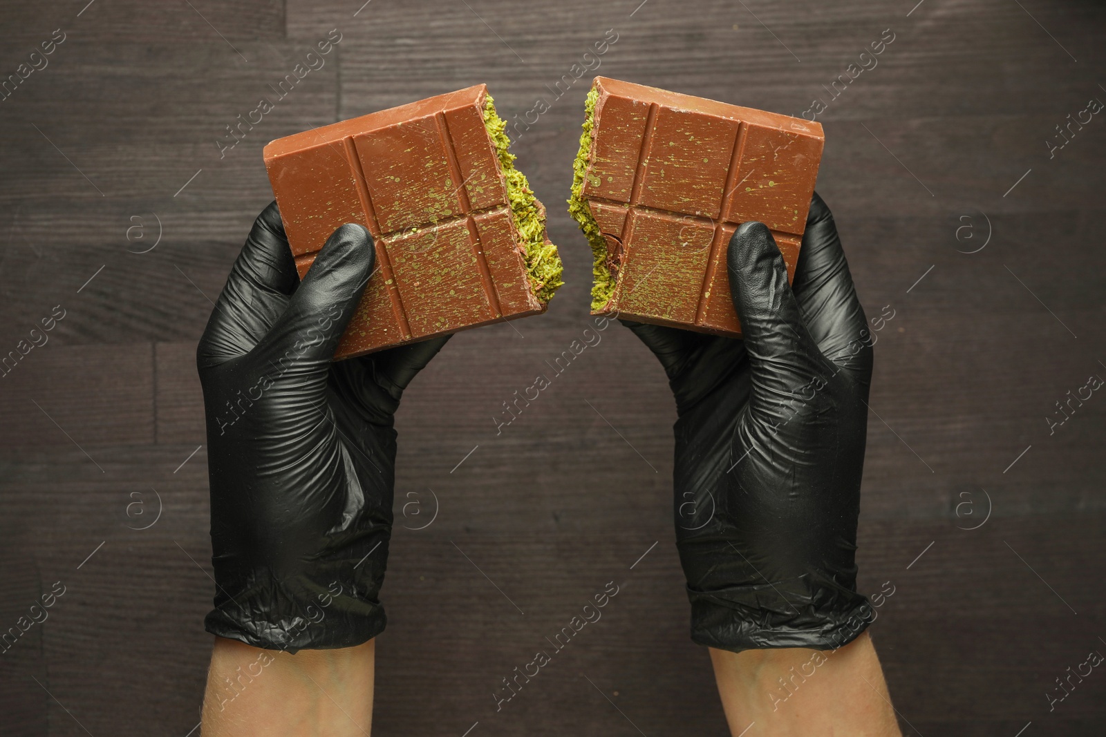 Photo of Woman breaking Dubai chocolate bar with pistachio and knafeh at wooden table, top view