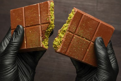 Photo of Woman breaking Dubai chocolate bar with pistachio and knafeh at dark table, closeup