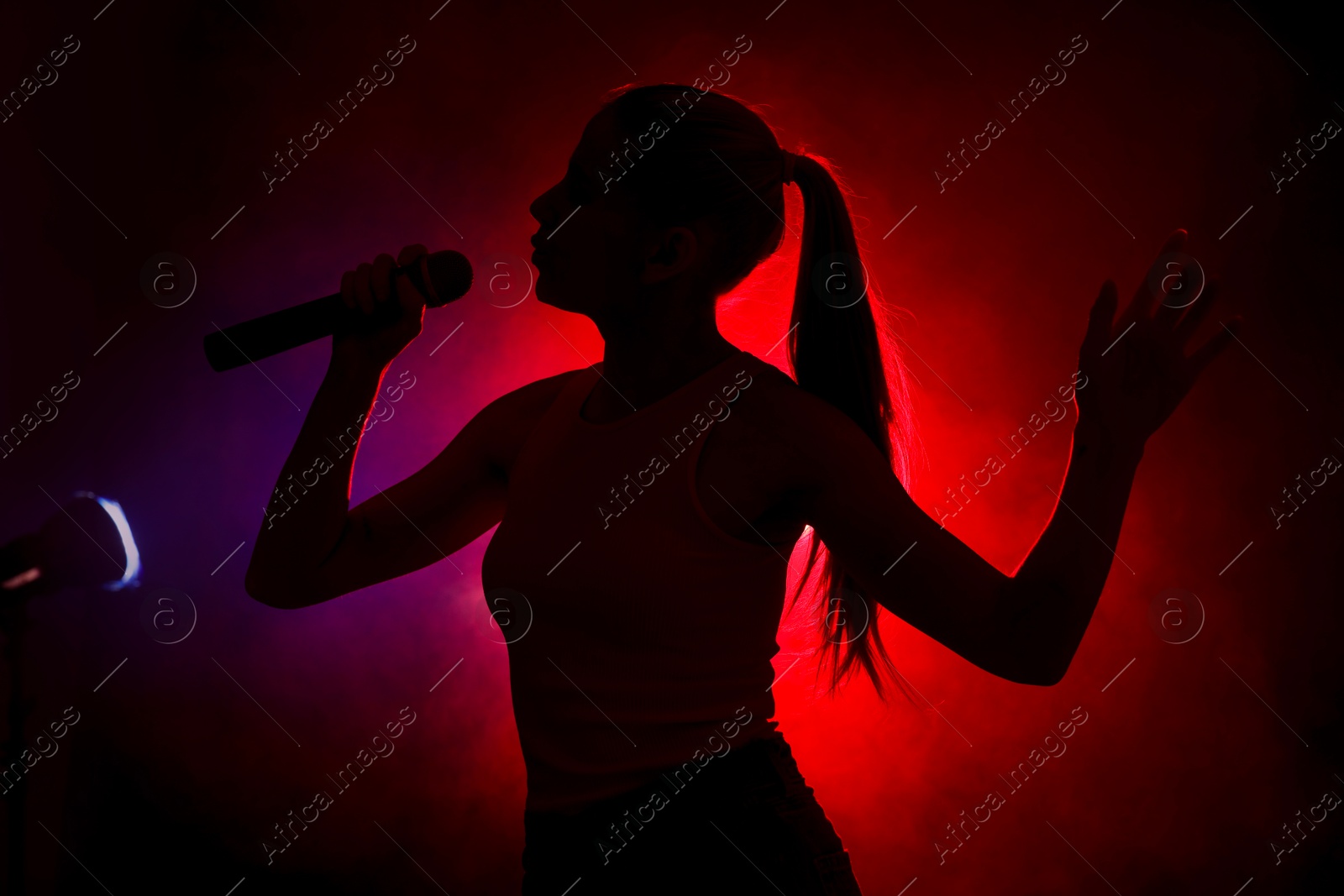 Photo of Silhouette of woman singing on dark background with color lights