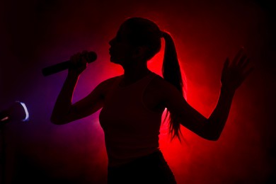 Photo of Silhouette of woman singing on dark background with color lights