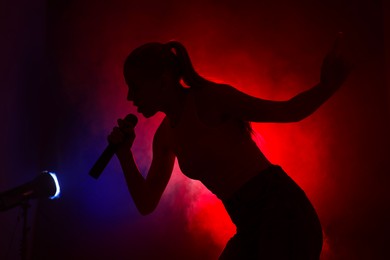 Photo of Silhouette of woman singing on dark background with color lights