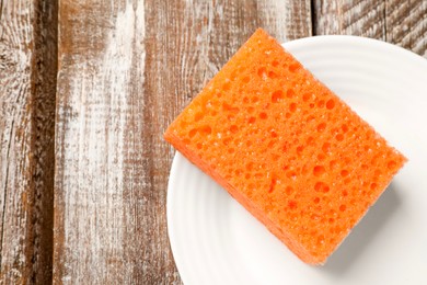 Photo of Orange sponge and plate on wooden table, top view. Space for text