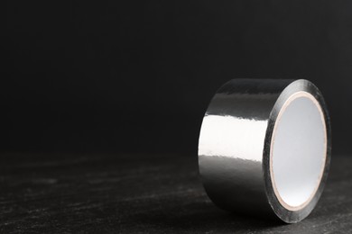 Roll of silver adhesive tape on black table, closeup. Space for text