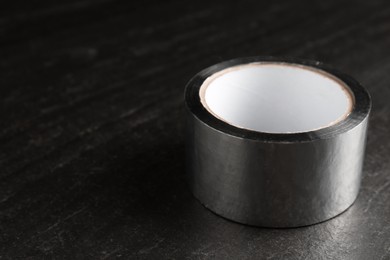 Photo of Roll of silver adhesive tape on black table, closeup. Space for text