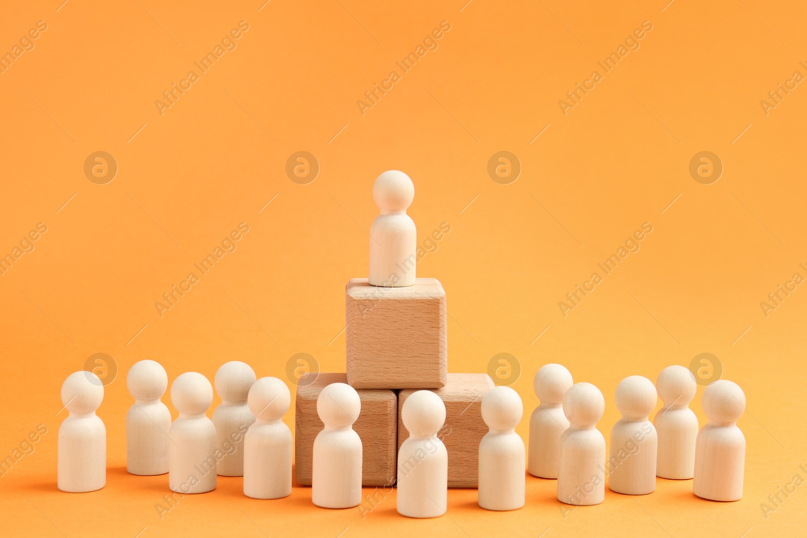 Photo of Human figures near stacked wooden cubes with one figure on top against orange background. Competition concept