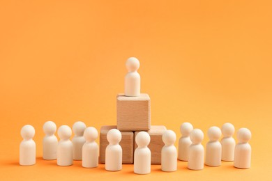 Photo of Human figures near stacked wooden cubes with one figure on top against orange background. Competition concept