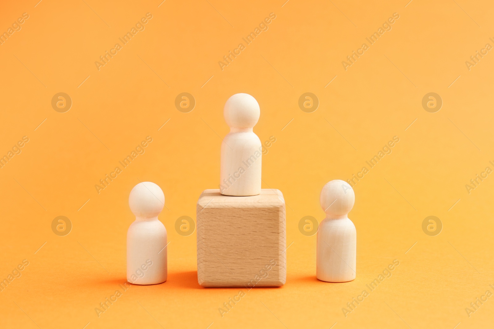 Photo of Human figures near cube with wooden figure against orange background. Competition concept