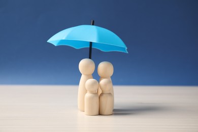 Photo of Human figures under umbrella on white table against blue background. Insurance concept