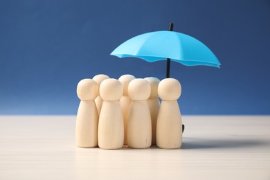 Photo of Human figures under umbrella on white table against blue background. Insurance concept