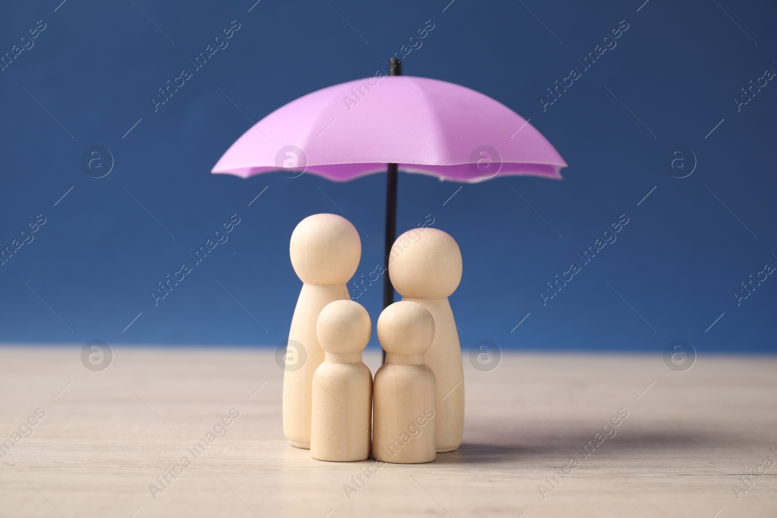 Photo of Human figures under umbrella on light wooden table against blue background. Insurance concept