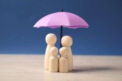 Photo of Human figures under umbrella on light wooden table against blue background. Insurance concept