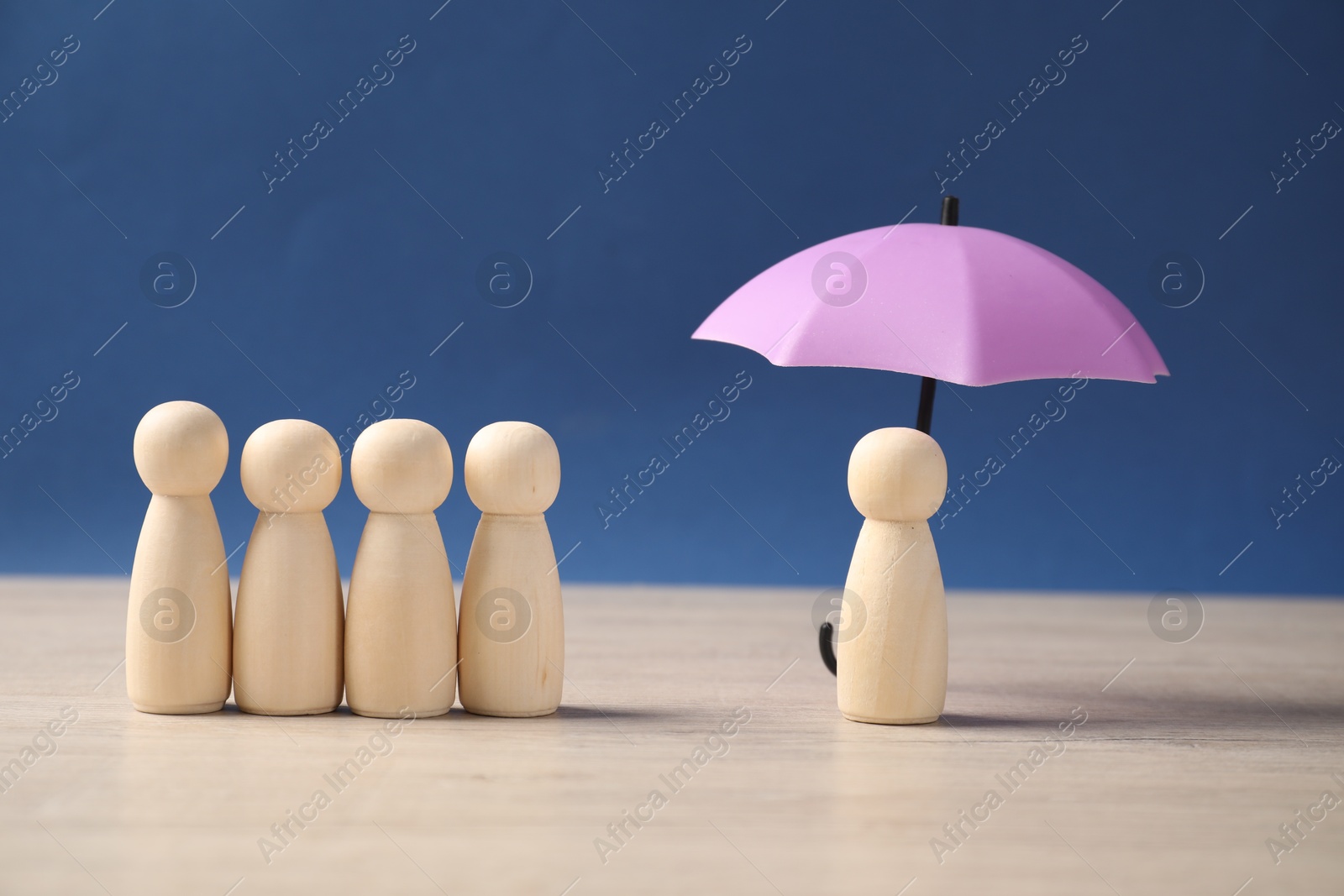 Photo of Human figure under umbrella and wooden ones on light table against blue background. Insurance concept