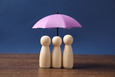 Photo of Human figures under umbrella on wooden table against blue background. Insurance concept